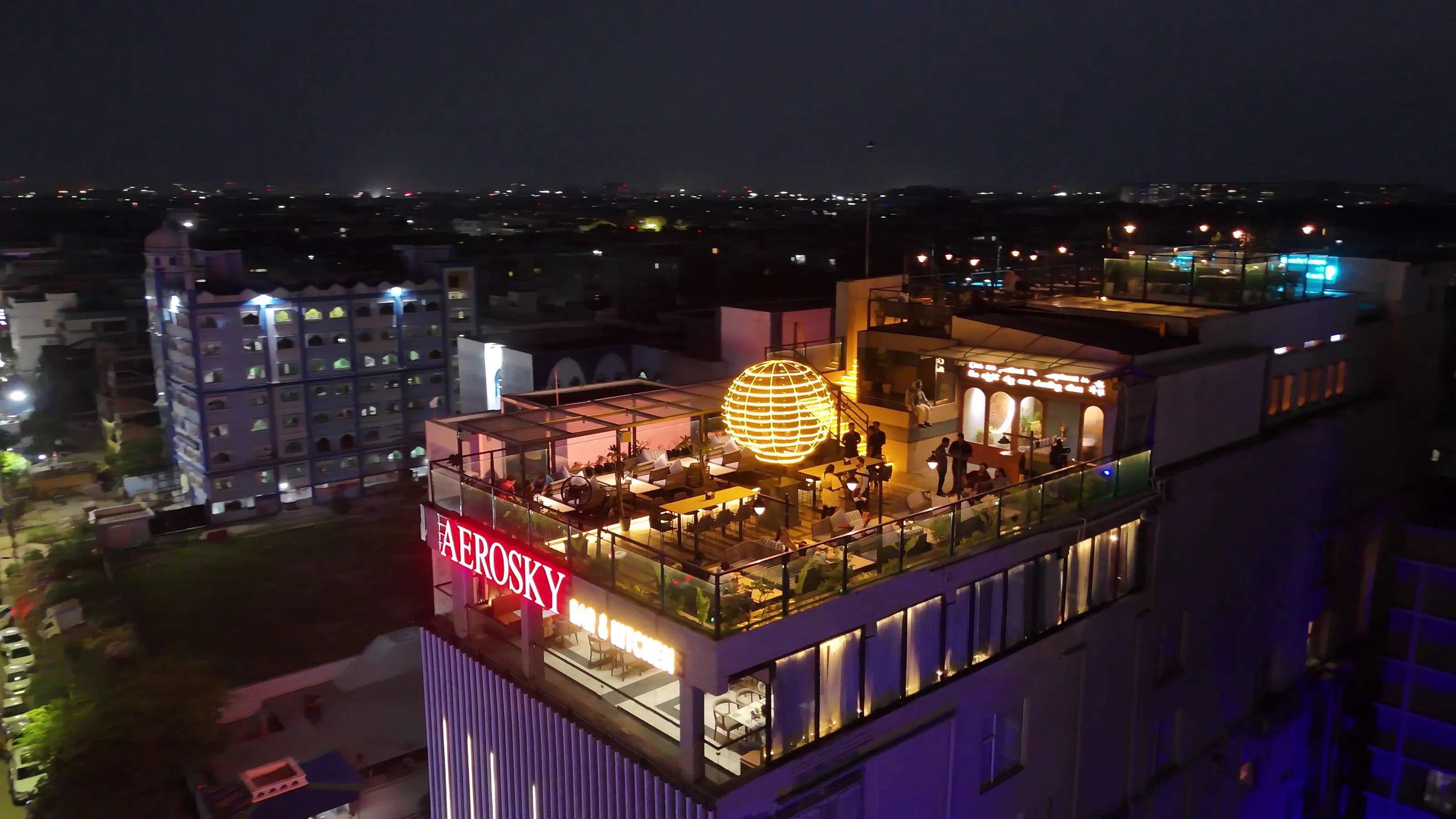 Aerosky at night from the air — the lit balloon sculpture on the tenth-floor roof, the Aerosky sign on the parapet, and Kolkata spreading out behind