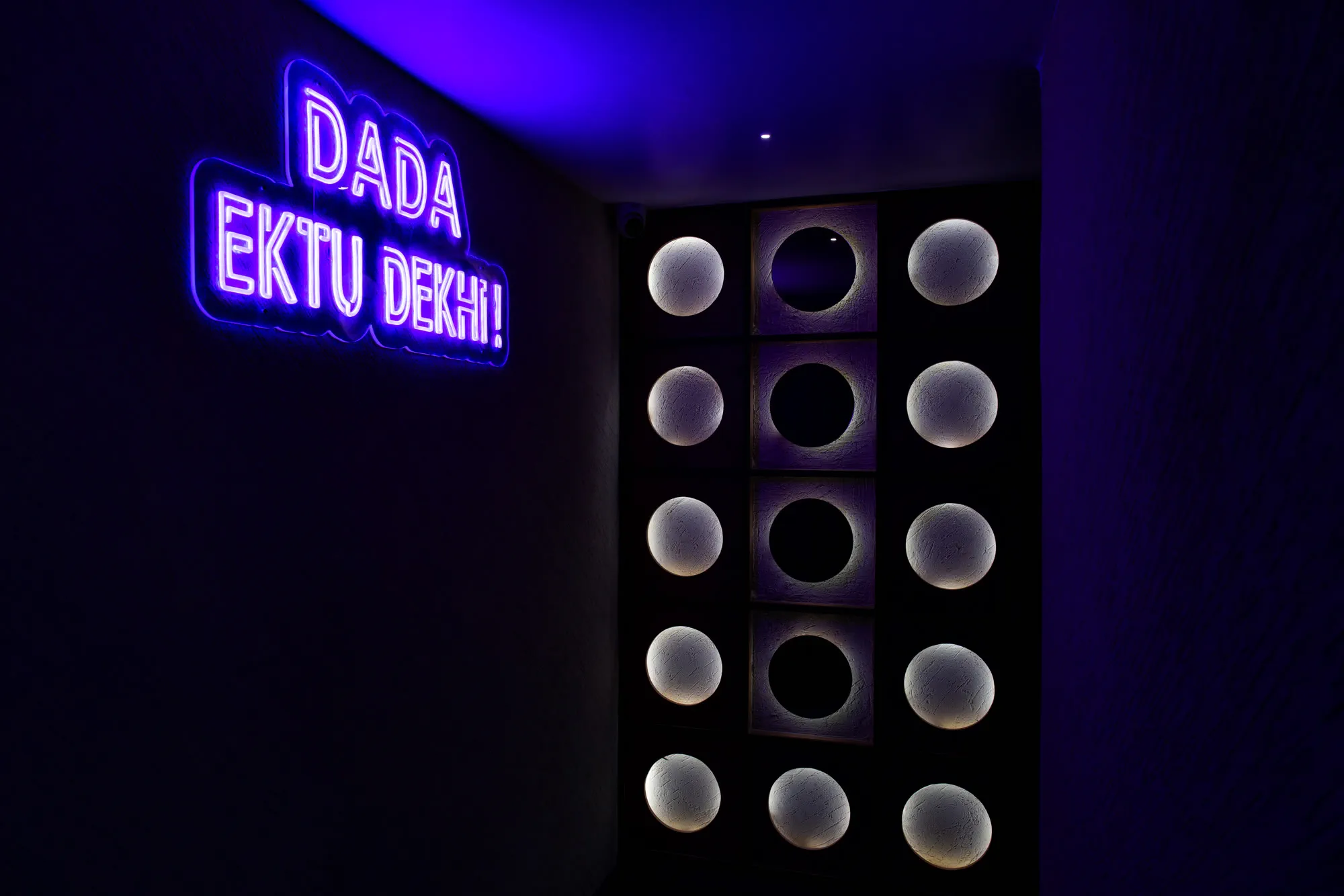 The washroom corridor, with neon lettering and backlit circular relief panels