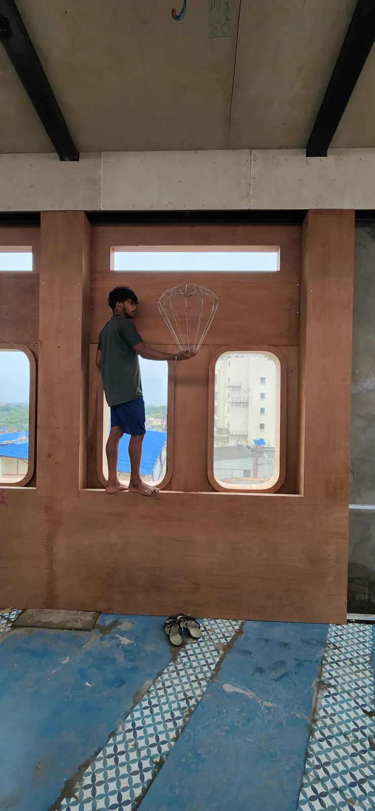 A balloon pendant's wire frame held up against the plywood porthole wall