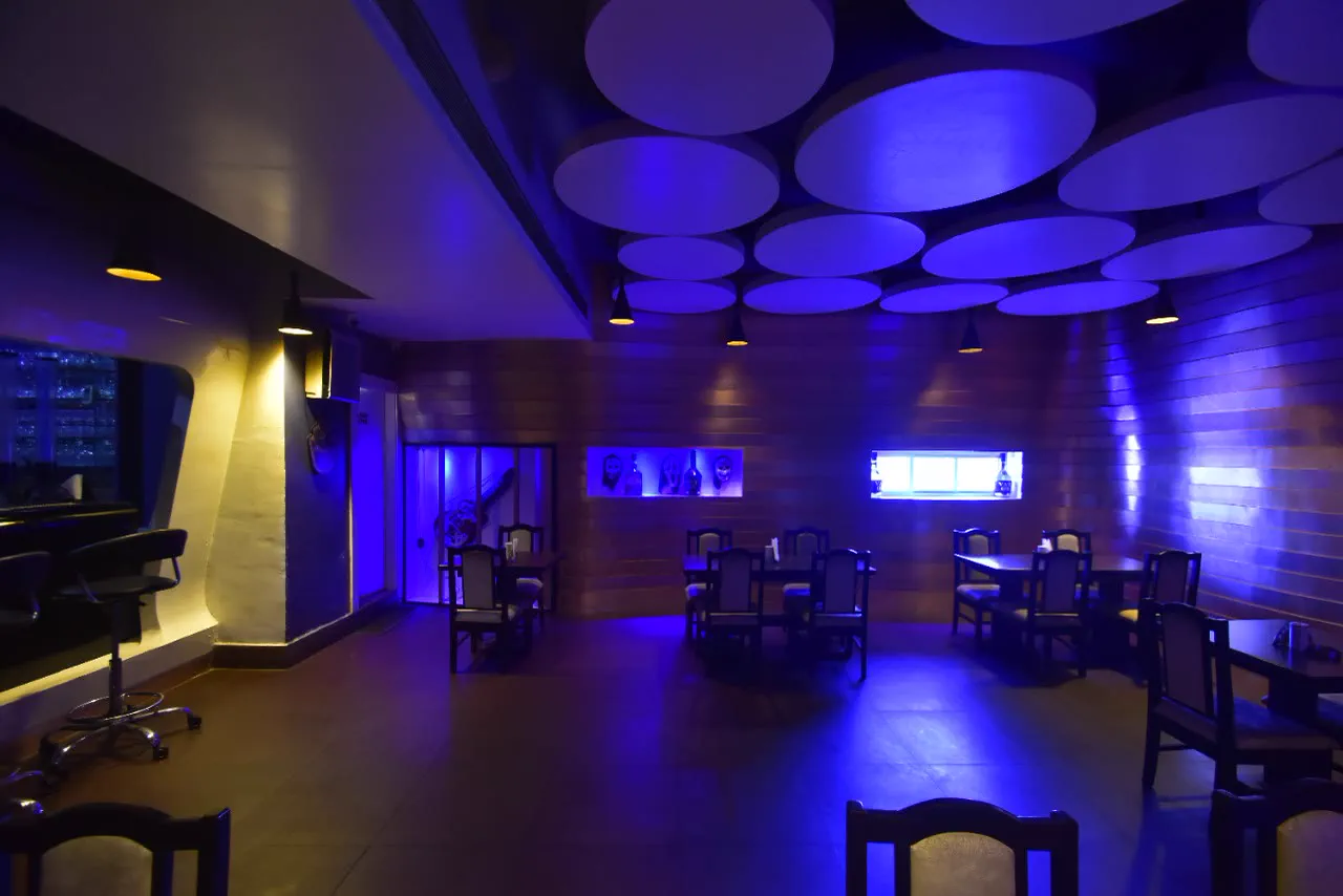 The existing bar before work: timber-lined walls, a ceiling of circular acoustic discs lit blue, loose dark chairs and tables