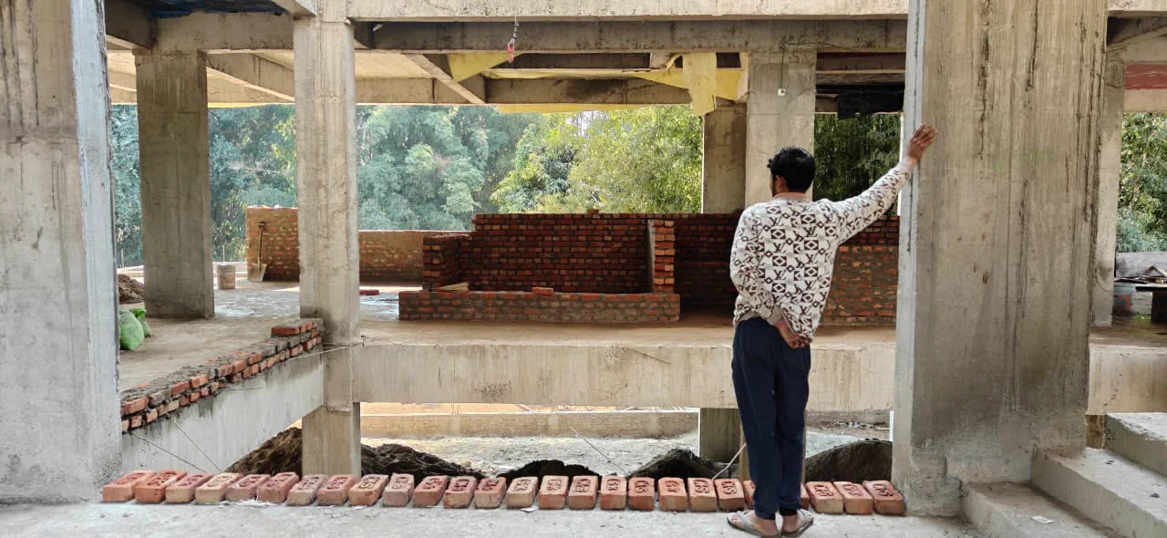 First floor interior during construction, brick infill walls rising between columns with bricks laid out in rows across the slab