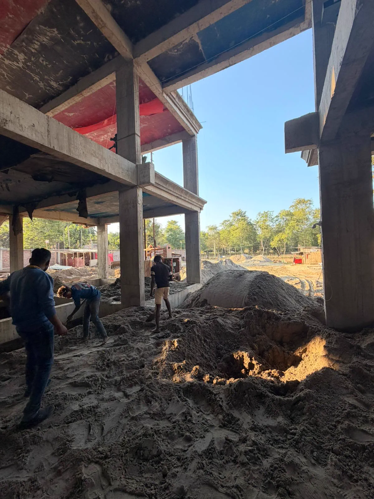 Inside the concrete frame at the double-height living space, floor still heaped with sand, workers spreading it