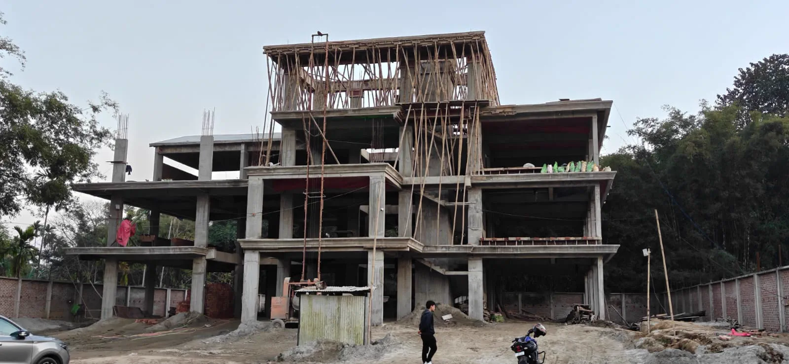 Wide view of the completed concrete frame with bamboo scaffolding, the stepped massing and projecting roof already visible