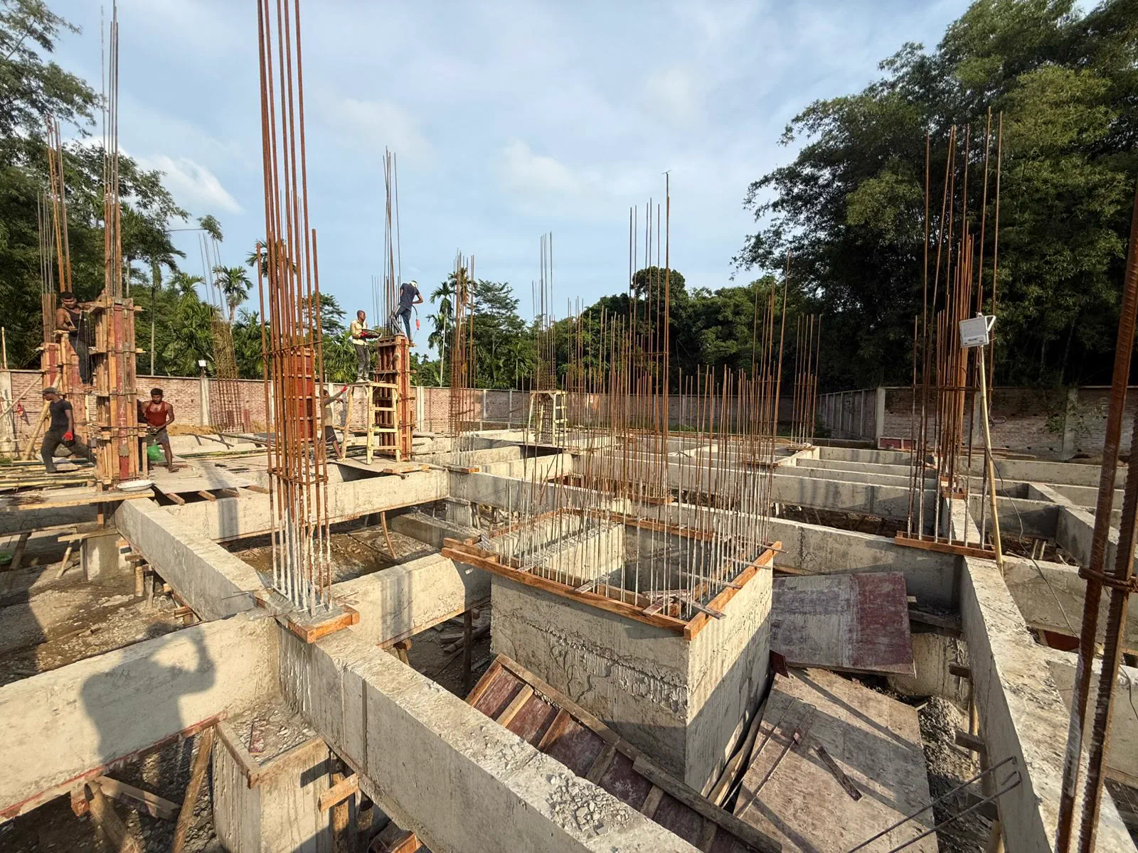 The full grid of plinth beams and column starters across the site, with workers placing reinforcement