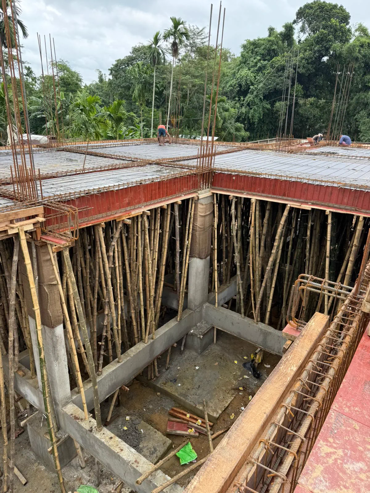 Looking down into the frame at a forest of bamboo props supporting the slab formwork, with the courtyard void open through the middle