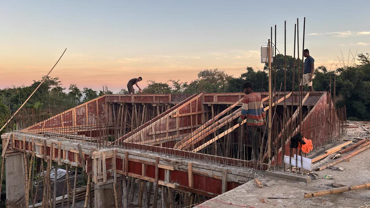 Workers forming the sloping off-centre bedroom roof in shuttering at dusk, bamboo props beneath