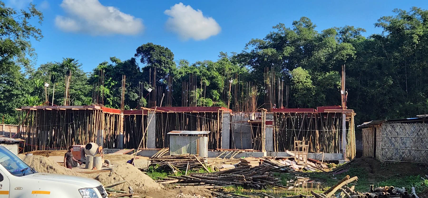 Panoramic view of shuttering for the ground floor slab carried on dense bamboo propping, mixer and stacked bamboo in the foreground