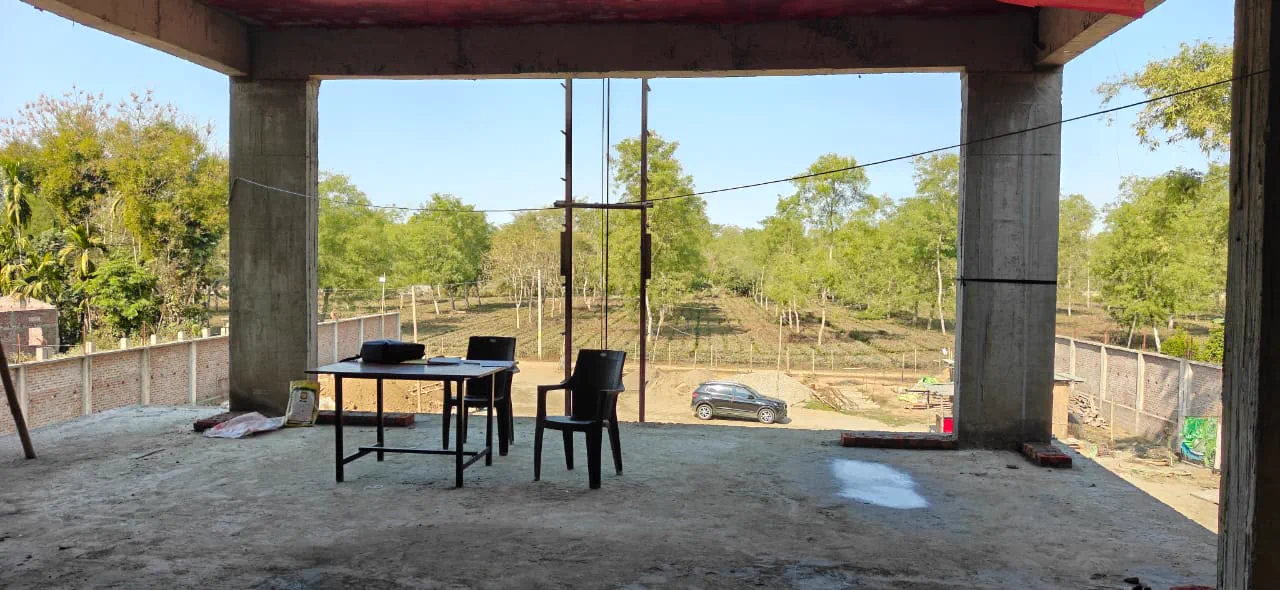 View out from the first floor covered balcony over a tea estate with shade trees, a table and chairs set up in the unfinished room