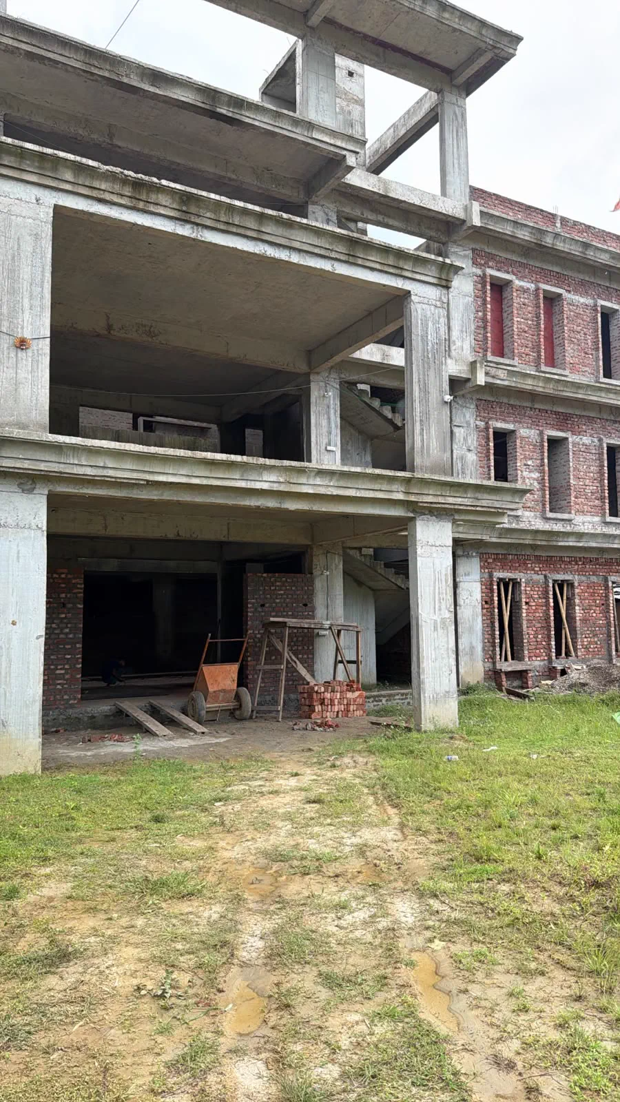 The bare concrete frame of the house in front, with the office block behind it already carrying red brick infill