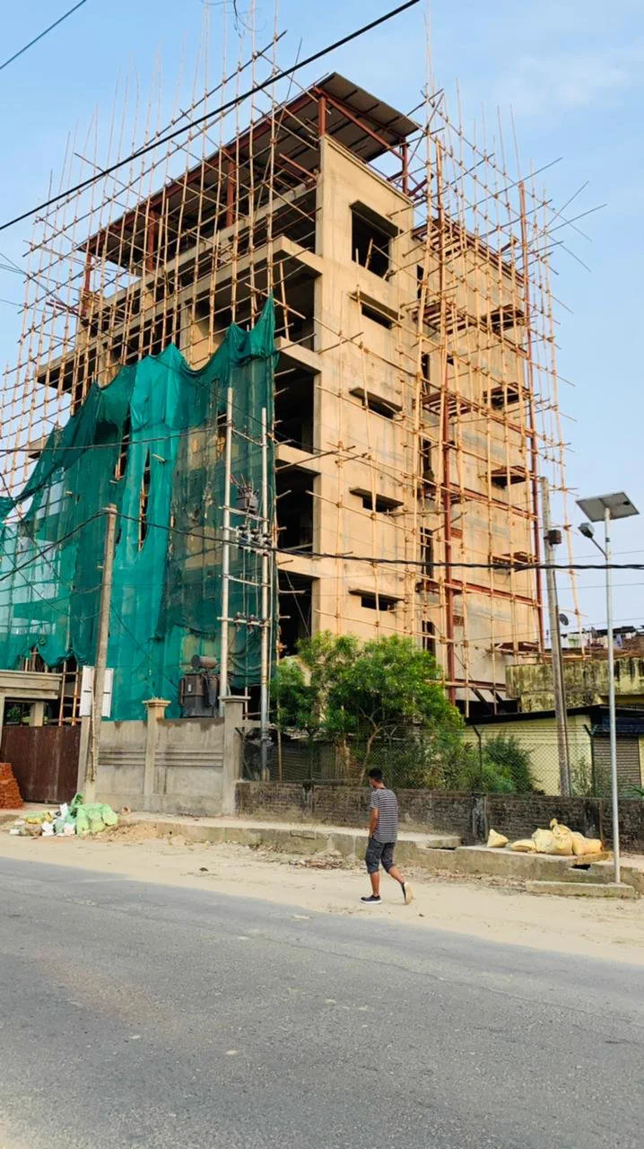 The building under construction, wrapped in bamboo scaffolding and green netting