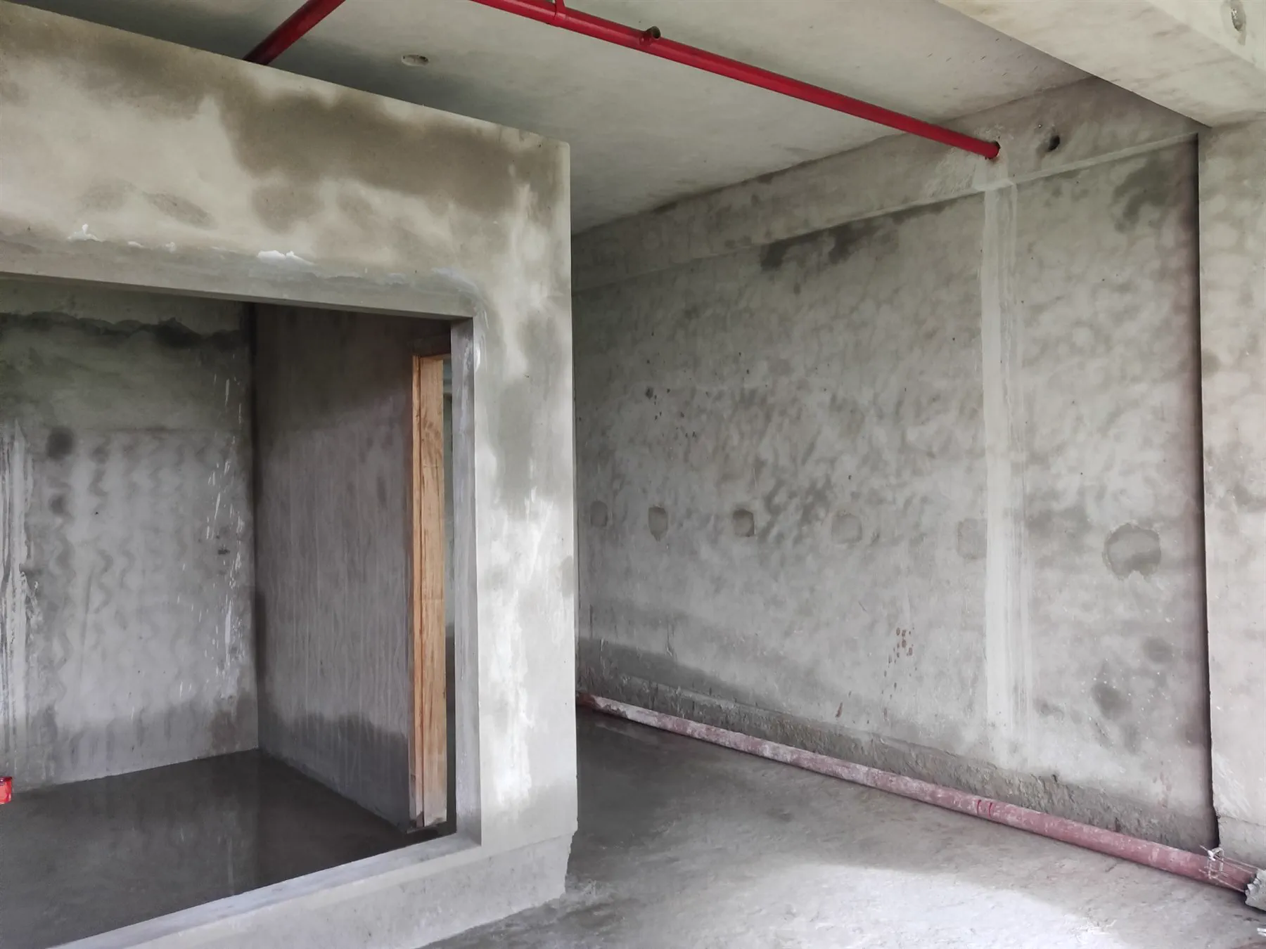 A bare concrete guest room during construction with sprinkler pipework overhead