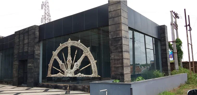 The building from outside, a carved stone Konark wheel set against the dark glazed facade