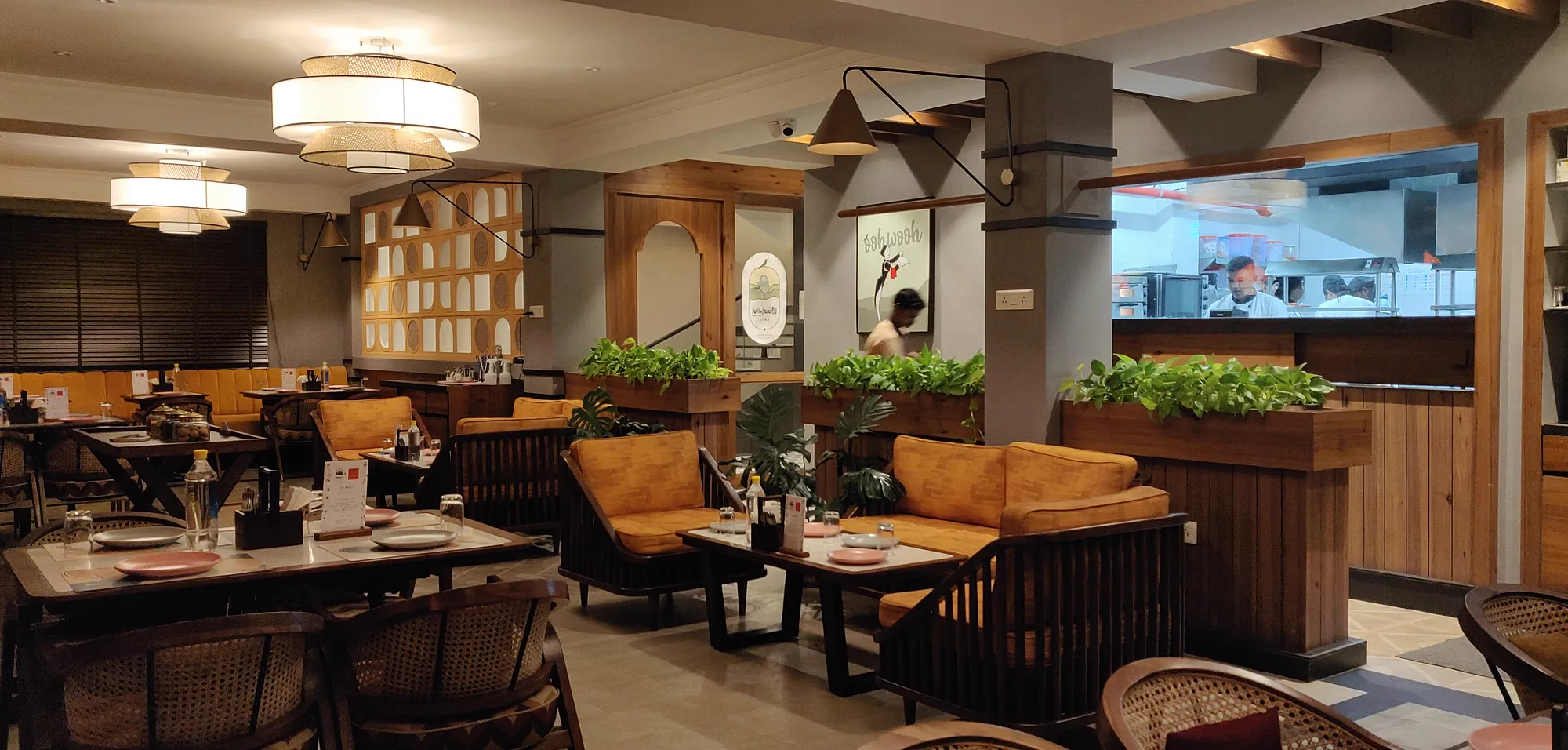The Windsong Cafe dining room as built &mdash; timber sofas and mustard cushions, planters of pothos, and the open kitchen counter beyond